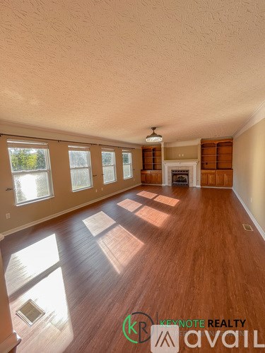 A room with wooden floors and a large window with sunlight coming through.