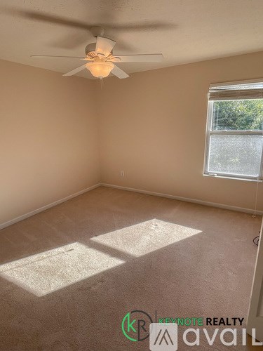A room with a ceiling fan and a window letting in sunlight.