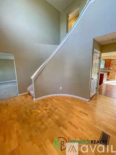 A wooden floor in a room with a staircase and a wall with a window.