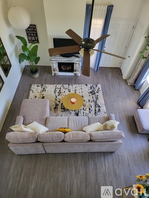 A living room with a grey couch, a coffee table, a ceiling fan, and a plant.