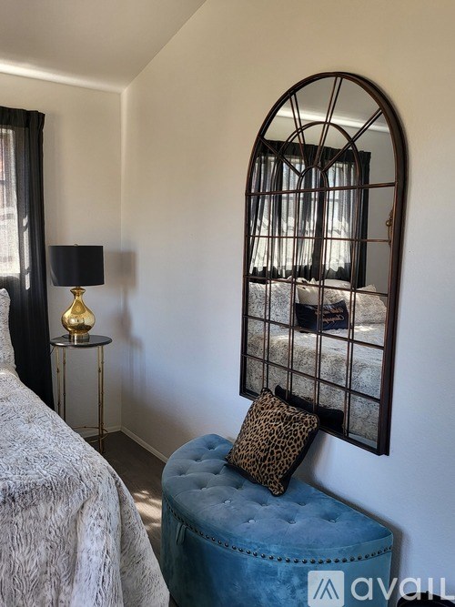 A bedroom with a bed, a lamp, a stool and a mirror.