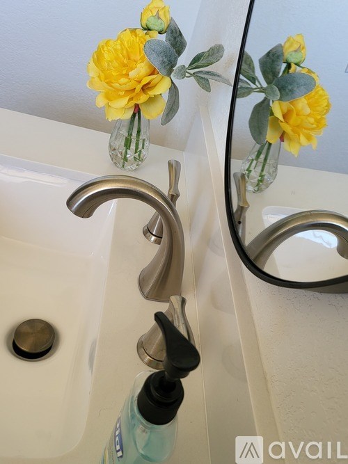 A bathroom sink with a yellow flower in a vase.