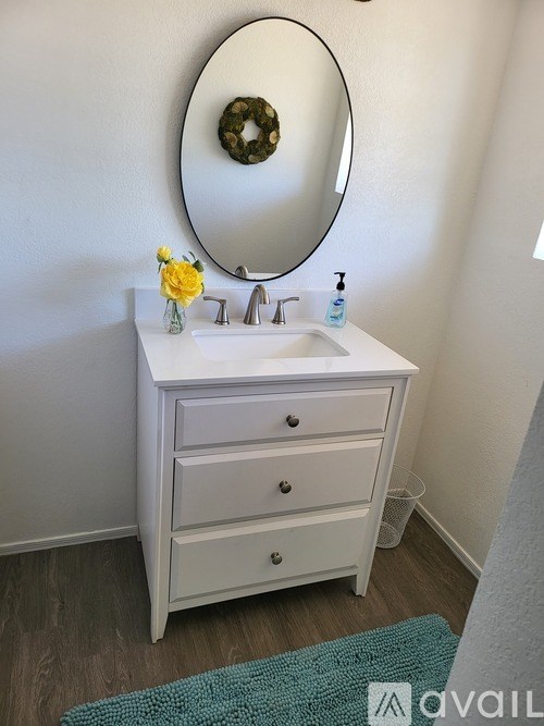 A white bathroom vanity with a round mirror and a yellow flower.