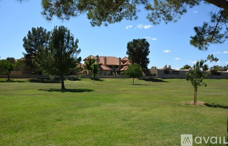 A grassy field with trees and houses in the background.