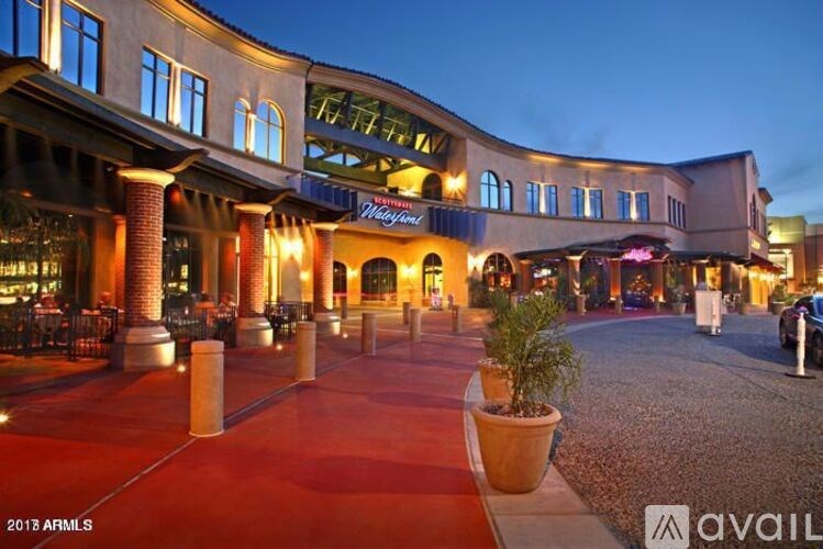 A shopping center with a red brick walkway and lit up storefronts.
