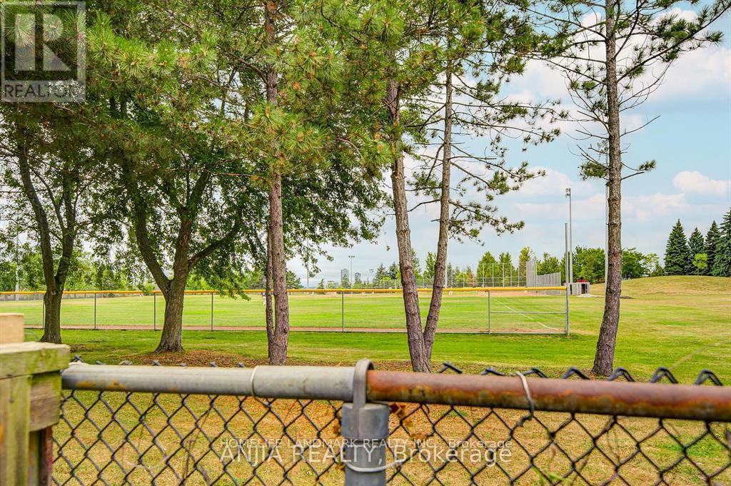 A chain link fence with a gate in front of a grassy field with trees.