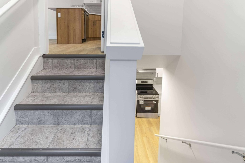 A staircase with a grey carpeted runner leads to a kitchen area.