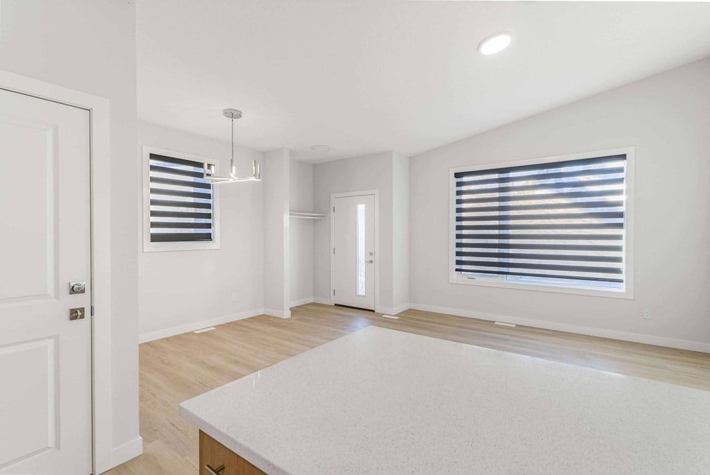 A white room with a bed in the middle and a window with blinds on the right side.