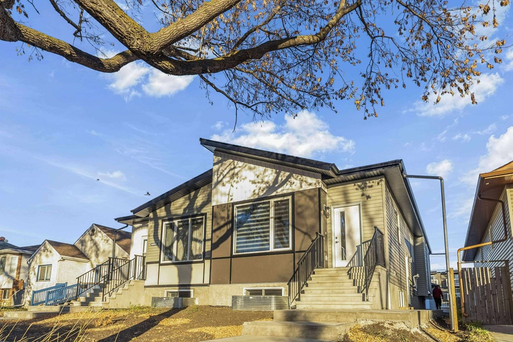 A house with a grey front and a tree branch in the foreground.