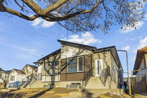 A house with a grey front and a tree branch in the foreground.