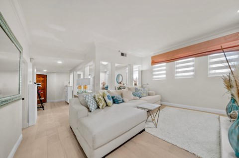 A white couch with blue and white pillows sits in a room with white walls and a white rug.