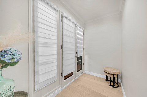 A room with a vase of flowers, a stool and a door with shutters.