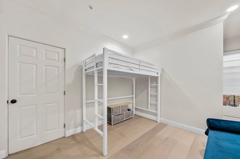A white bunk bed with a desk underneath it in a room with white walls.
