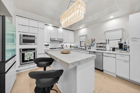 A modern kitchen with a marble island and black chairs.