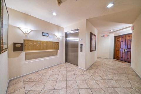 A hallway with a tiled floor, a wall of mailboxes, and a closed elevator.