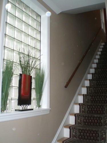 A staircase with a red vase and a window with a plant in front of it.