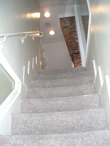 A staircase with a grey carpeted runner and white balusters.