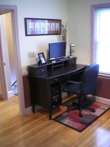A black computer desk with a chair and a monitor.