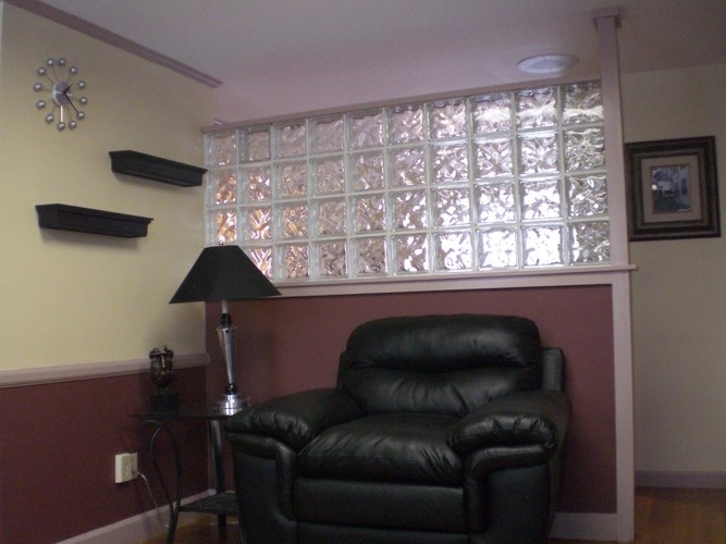 A black leather chair sits in front of a lamp and a window with a white frame.