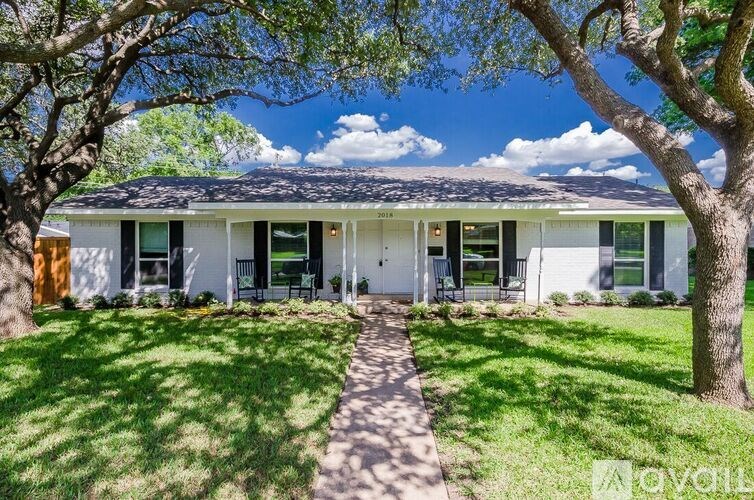 A white house with a black roof and a tree in front.