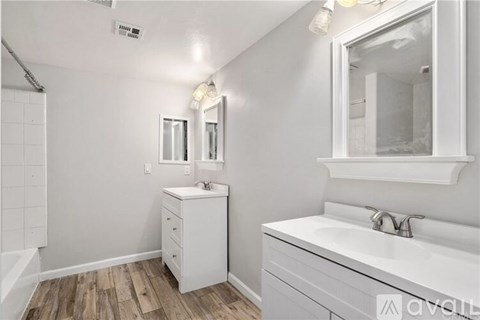 A white bathroom with a wooden floor and a white vanity.