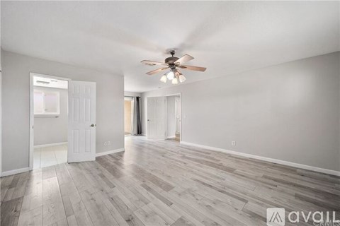 A spacious room with a ceiling fan and light, hardwood flooring, and white walls.