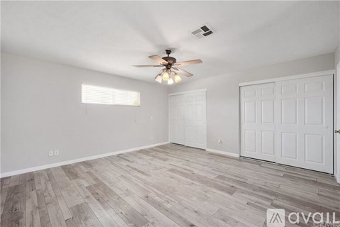 A room with a ceiling fan and light, wooden flooring, and two white doors.