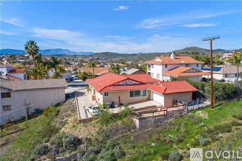 A house with a red roof is surrounded by other houses and vegetation.