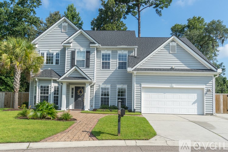 A house with a grey roof and white walls is surrounded by a green lawn and trees.