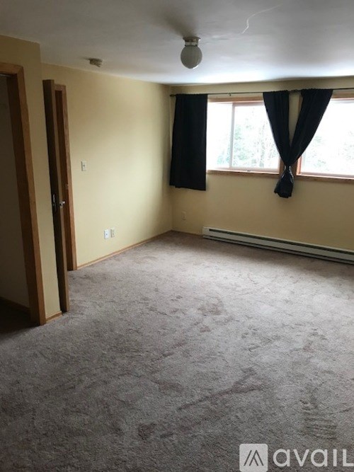 A room with a carpeted floor and a window with black curtains.