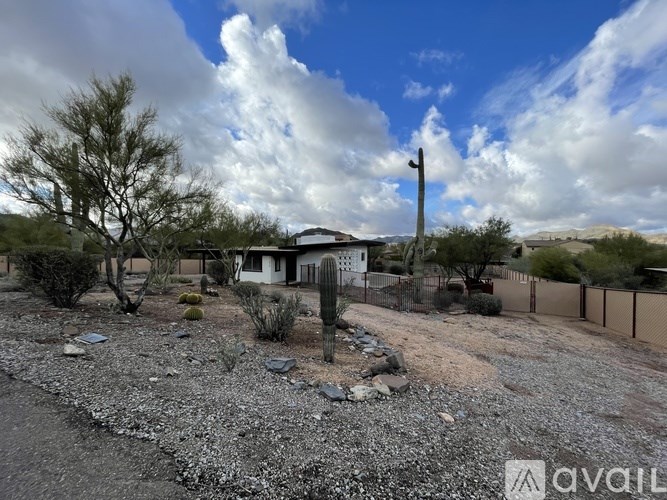 A gravel area with a house and trees in the background.