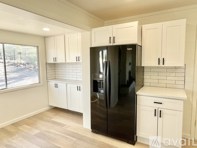 A kitchen with a black refrigerator, white cabinets, and a tiled backsplash.