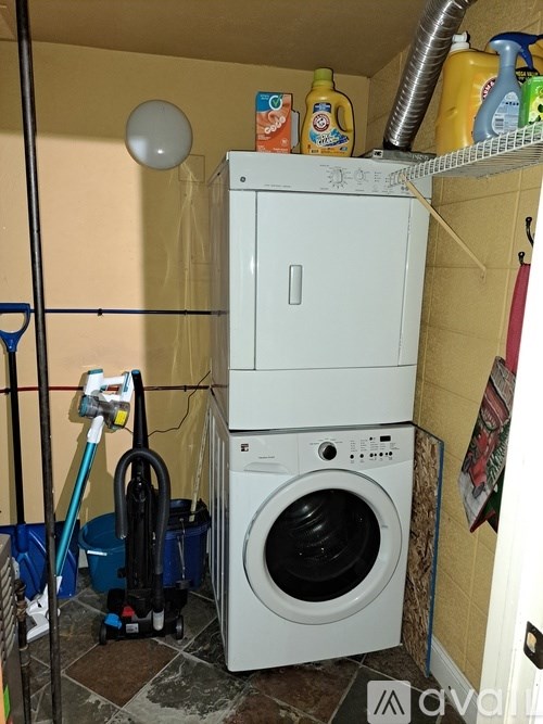 A white washing machine is stacked on top of a dryer in a small, cluttered laundry room.