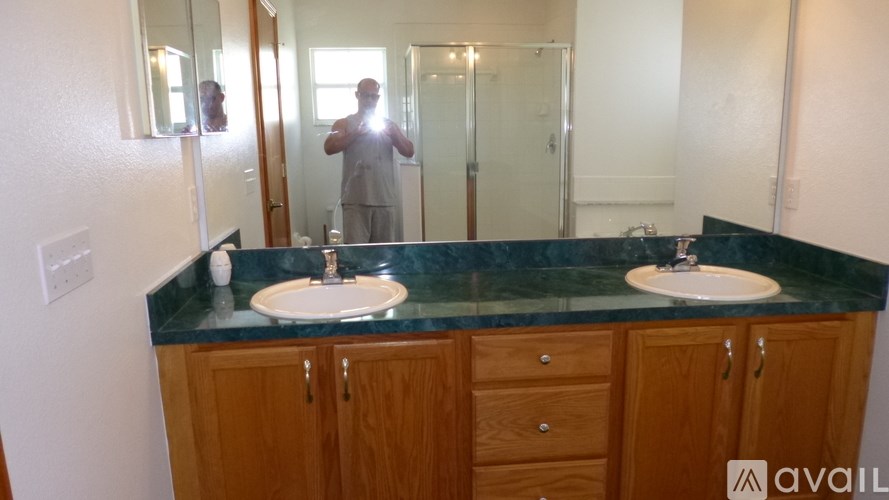 A man is taking a picture of a bathroom with a sink and mirror.