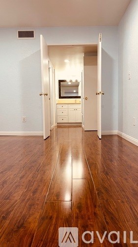 A room with a wooden floor and a kitchen in the background.