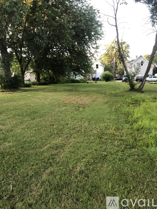 A grassy field with trees and houses in the background.
