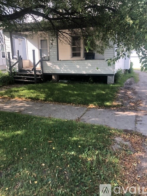 A small white house with a porch and a tree in front.