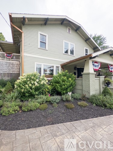 A house with a grey siding and a small front yard with bushes and a flag.