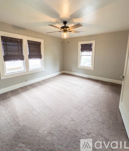 A room with a carpeted floor, a ceiling fan, and two windows.