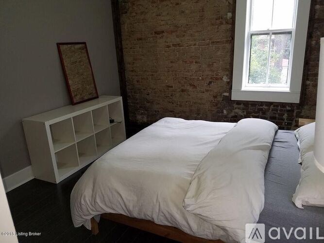 A bedroom with a white bed and a window with a view of greenery outside.