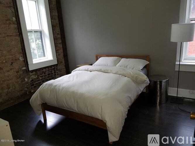A bed with white bedding sits in a room with a brick wall and a window.