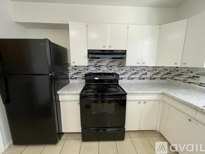 A black fridge and stove in a kitchen with white cabinets.