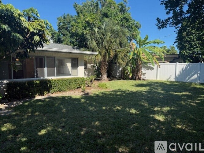 A house with a white fence and green trees in the backyard.