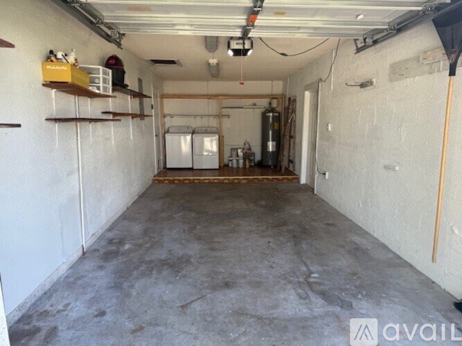 A spacious garage with a white floor and walls, containing a white refrigerator, a white washing machine, and a white dryer.