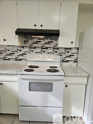 A white stove with a black burner is in a kitchen with white cabinets.