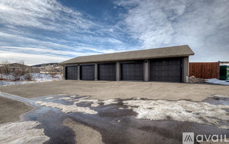 A large garage with a brown roof and a white door is surrounded by a snowy landscape.