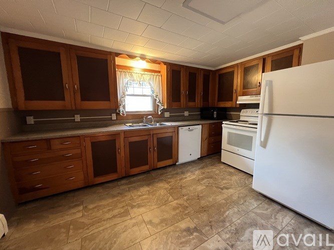 A kitchen with a white refrigerator, brown cabinets, and a tiled floor.