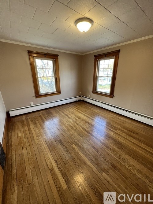 A room with wooden flooring and two windows.