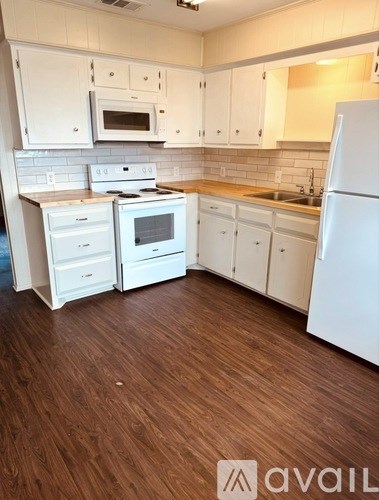 A kitchen with white appliances and wooden floors.