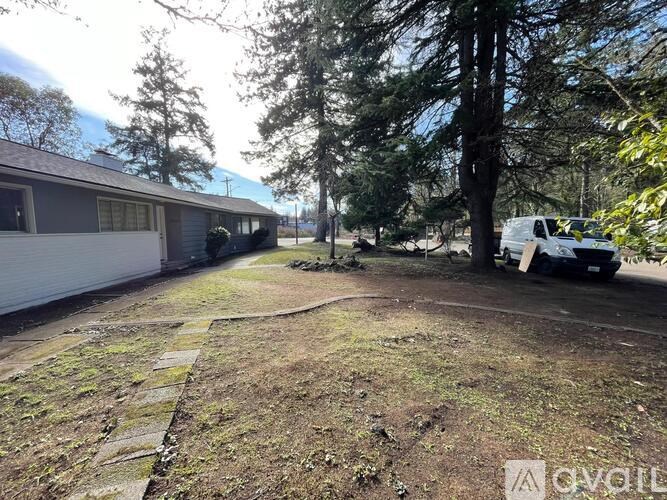 A backyard with a white house, a tree, and a white van.